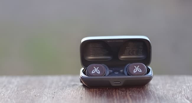 A pair of greyish blue Jaybird Vista earbuds on a wooden surface